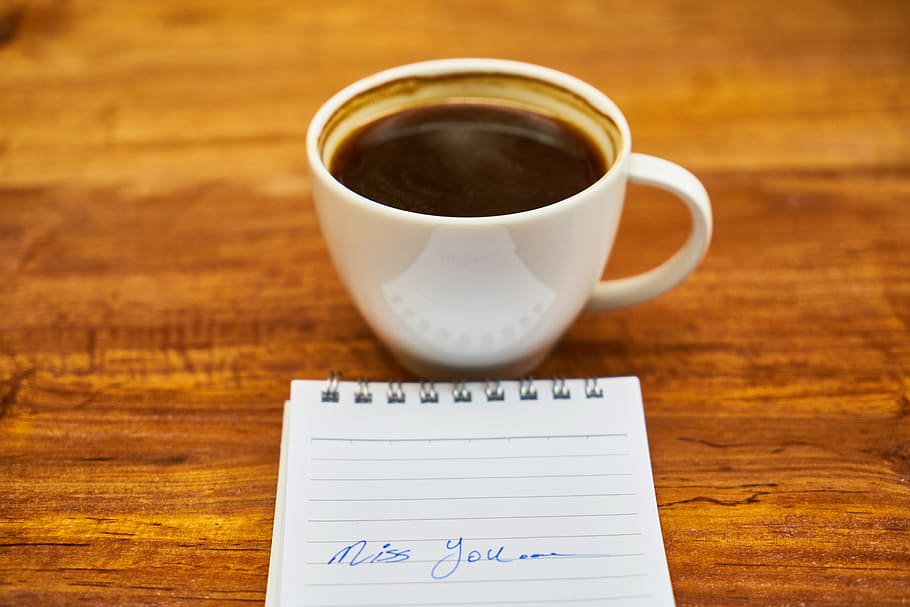 white ceramic cup beside black lined notebook on brown wooden surface