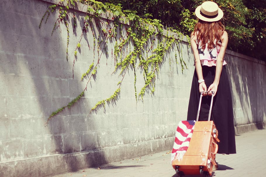 woman wearing a hat walking on a hallway pulling a luggage during daytime HD wallpaper