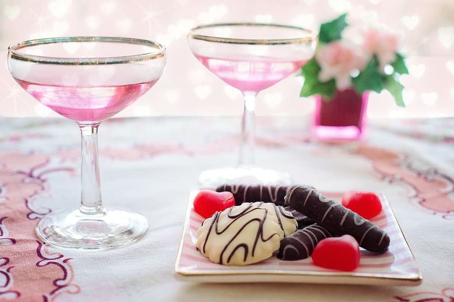 two wine glass beside vanilla and chocolate coated biscuit on plate