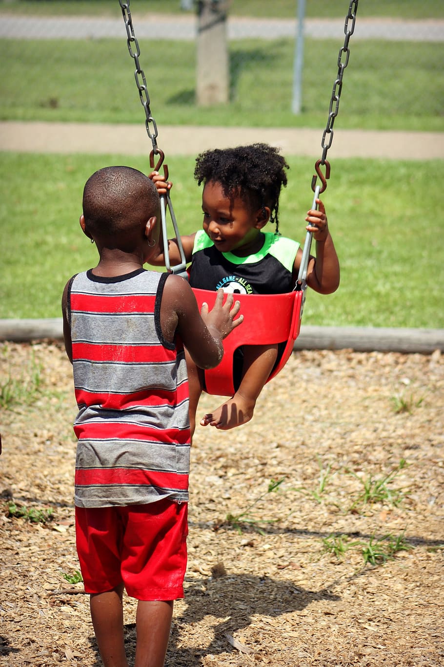 boy in red and black stripe tank top pushing red bucket swing chair HD wallpaper