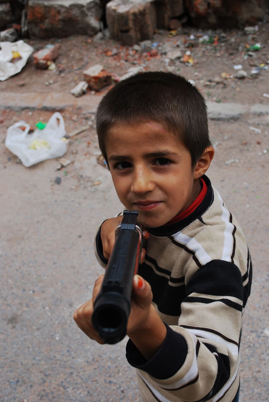 boy holding pistol toy, gun, pointing, smiling, trash, child
