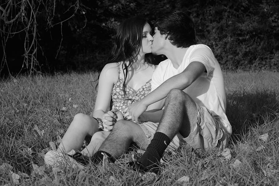 grayscale photo of couple sitting on grass while kissing, man