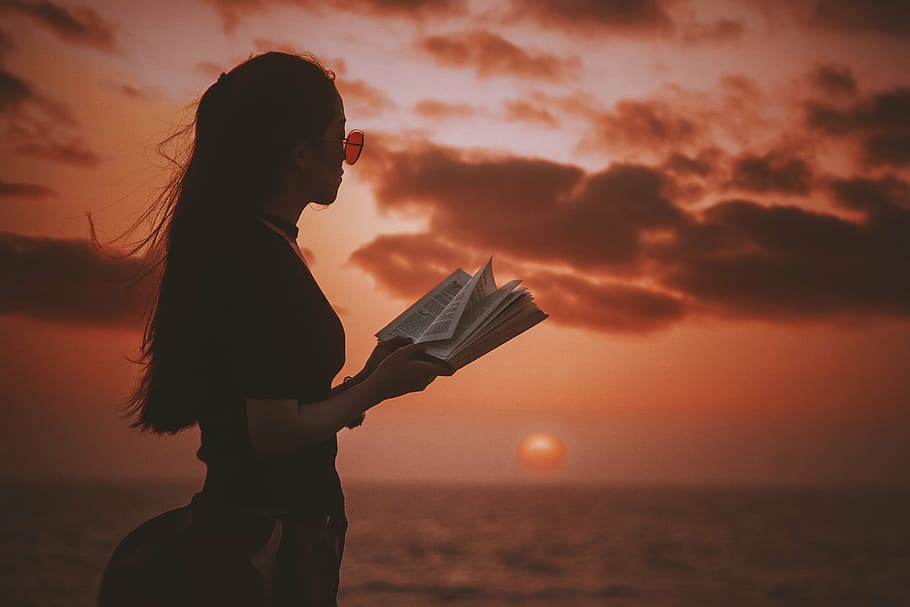 selective focus photo of woman holding book during golden hour HD wallpaper