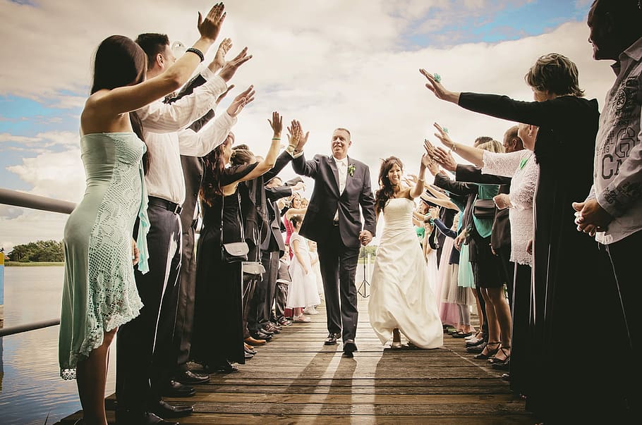 groom and bride walking on isle while giving high-five under white cloudy skies at daytime HD wallpaper