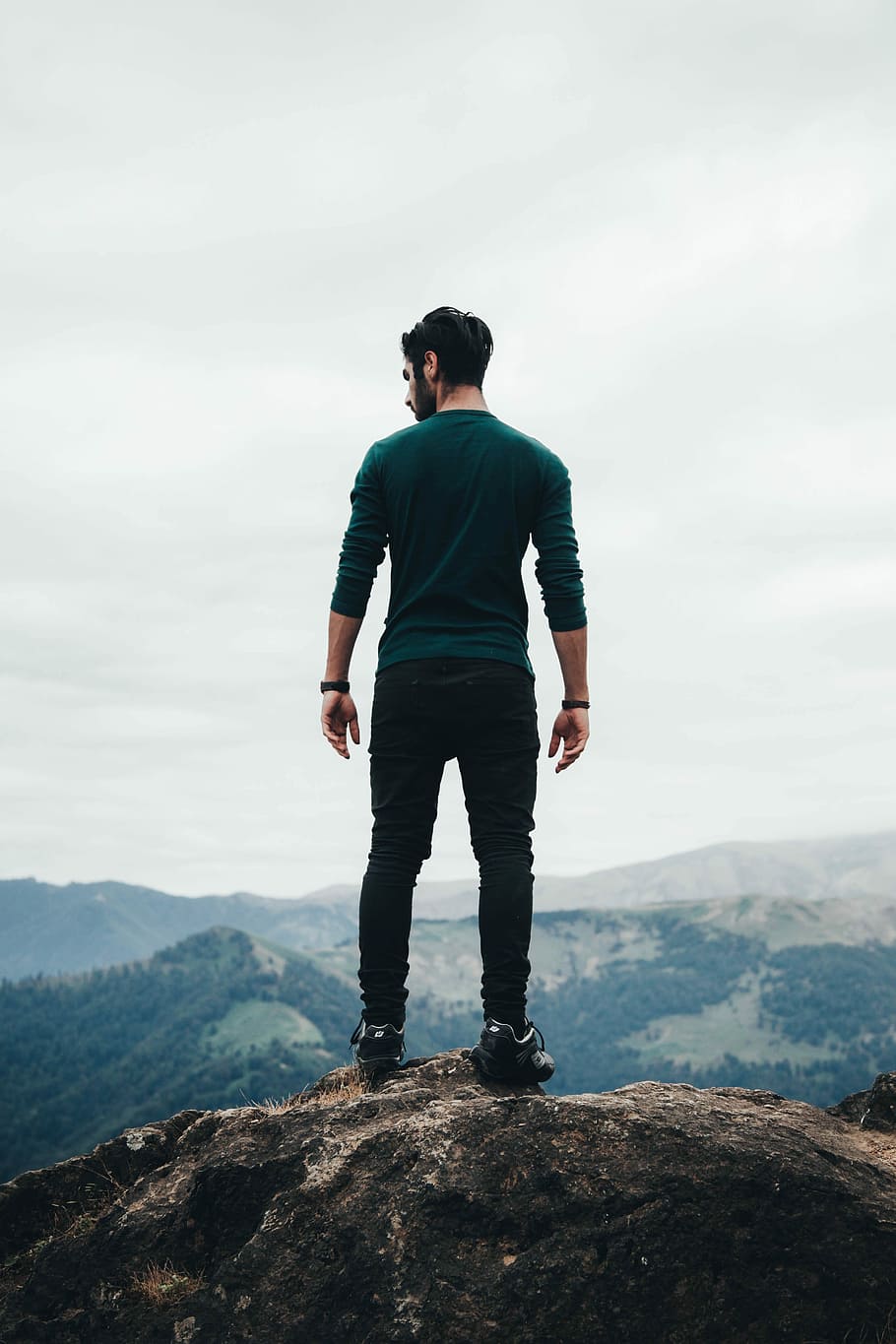 man standing on rock formation, man standing on rocky mountain under white sky during daytime HD wallpaper
