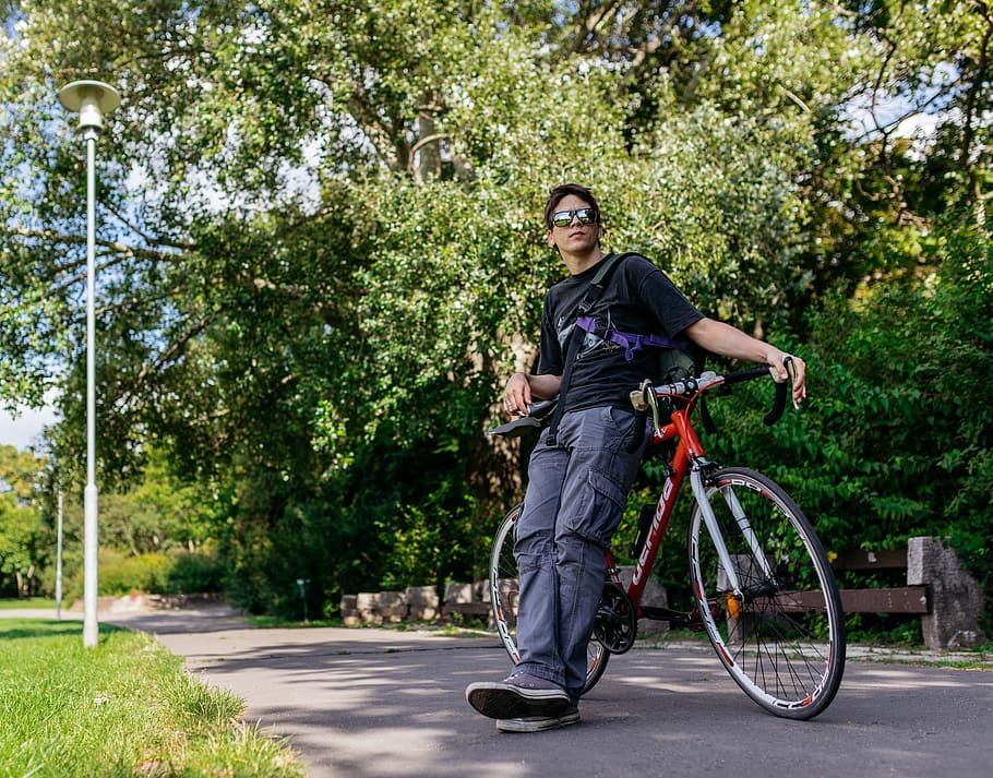 man leaning on red road bike on road under green leaf tree HD wallpaper