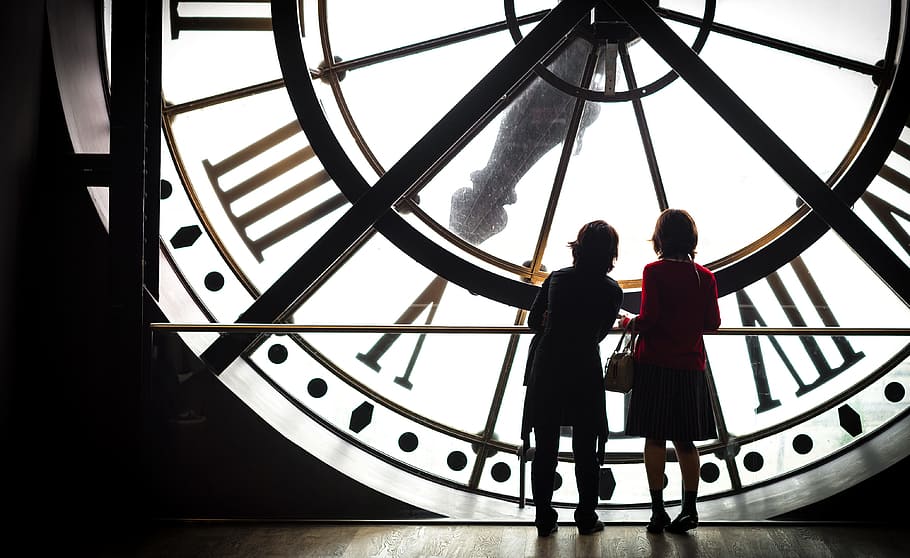 silhouette view of two women standing in front of big clock HD wallpaper