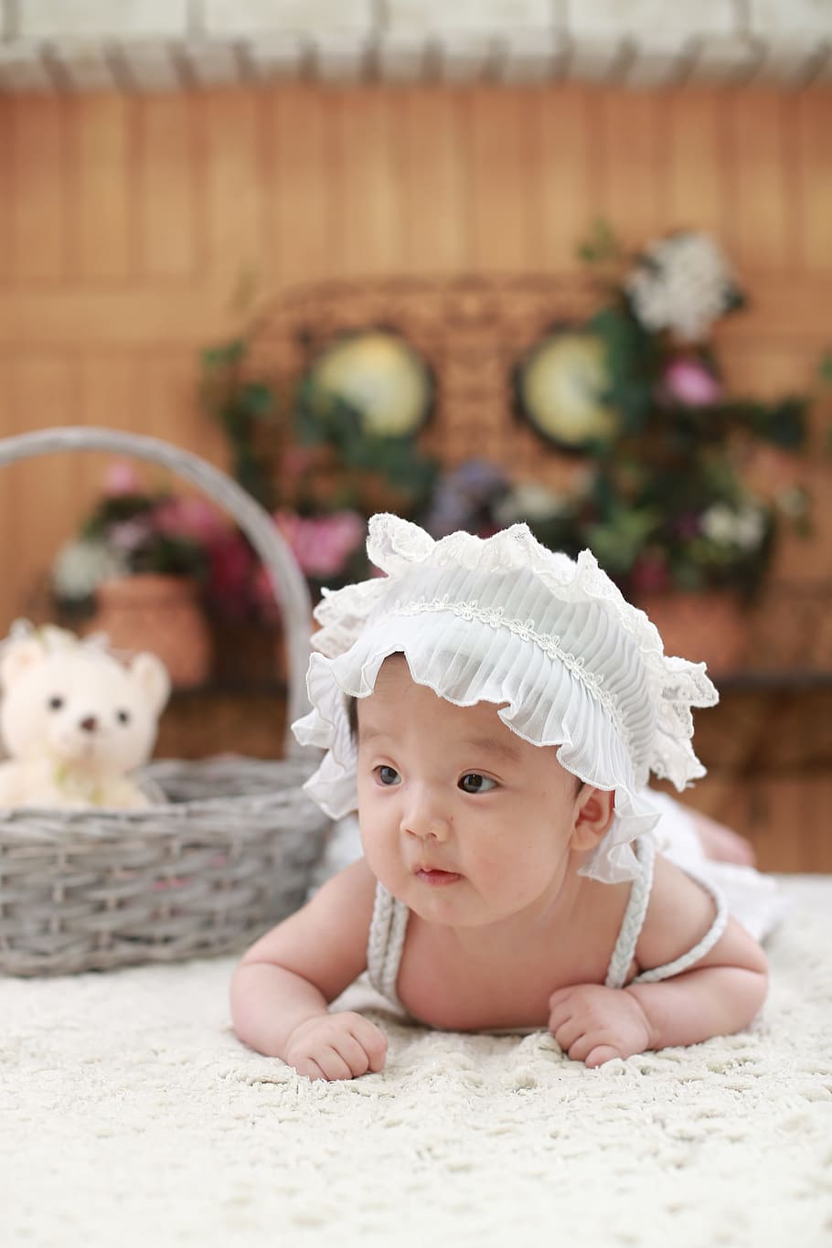 baby wearing white headdress beside gray wicker basket, Cute