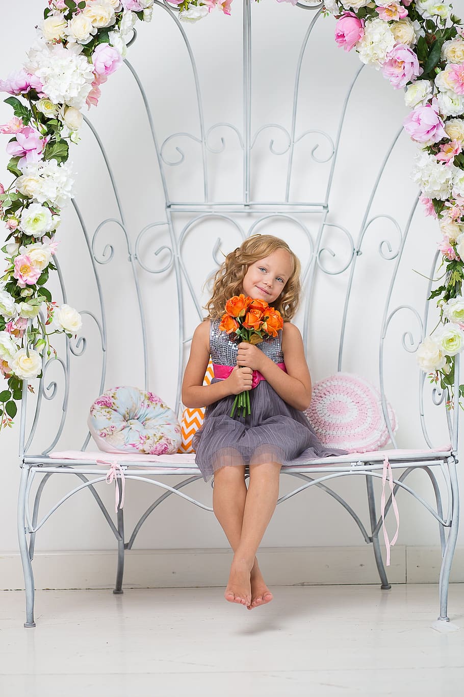 girl holding flowers wearing dress sitting on floral bench, child