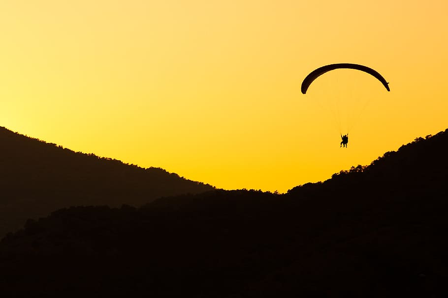 silhouette of person parachuting near valley during sunset, active