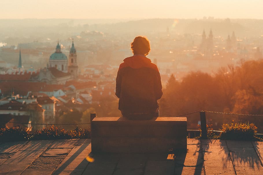 person sitting on brown bench, person sitting on brown wooden bench facing through city during sunset