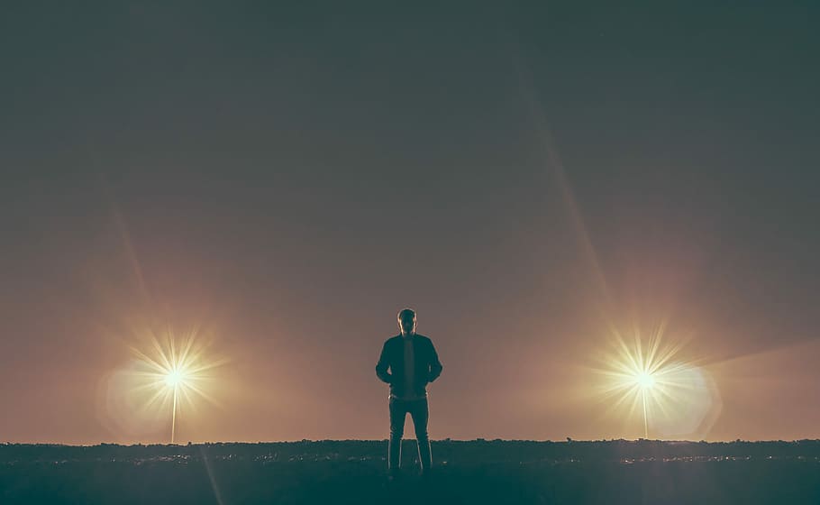 man standing in the middle of nowhere, man standing on ground with two lights turned on HD wallpaper