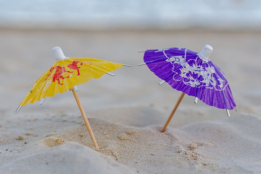 micro photography of two assorted-color mini umbrellas on sand HD wallpaper