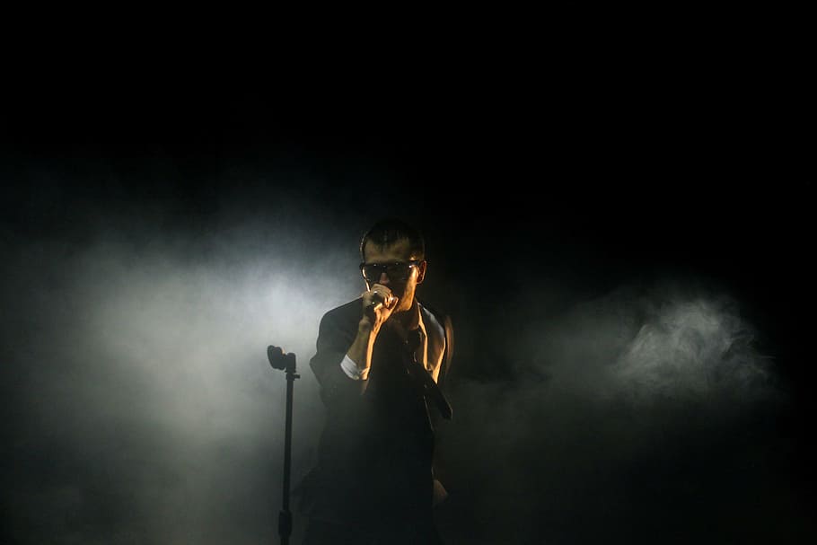 man wearing black suit holding microphone, concert, dark, light