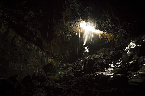 man walking on brown cave racks, person under cave, rock, night HD wallpaper