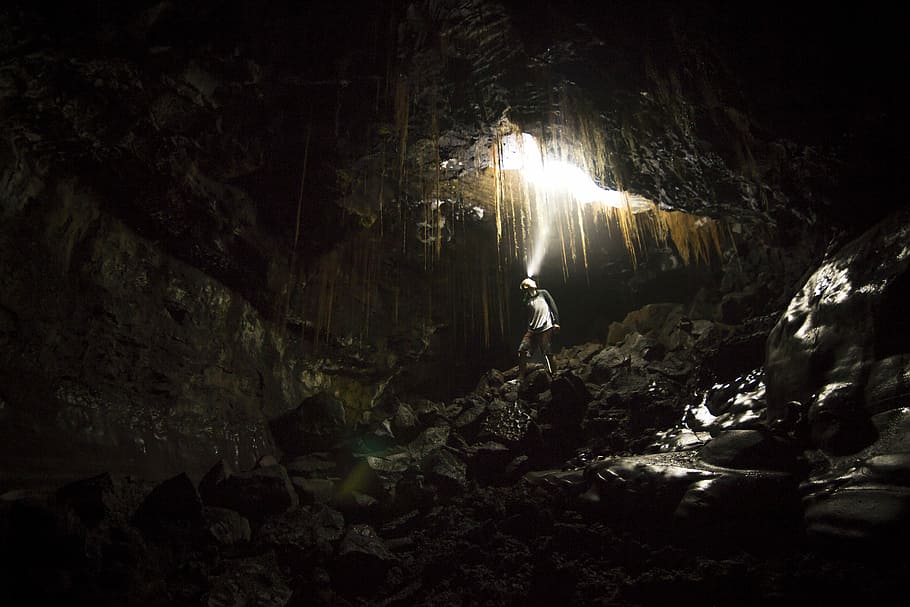 man walking on brown cave racks, person under cave, rock, night HD wallpaper