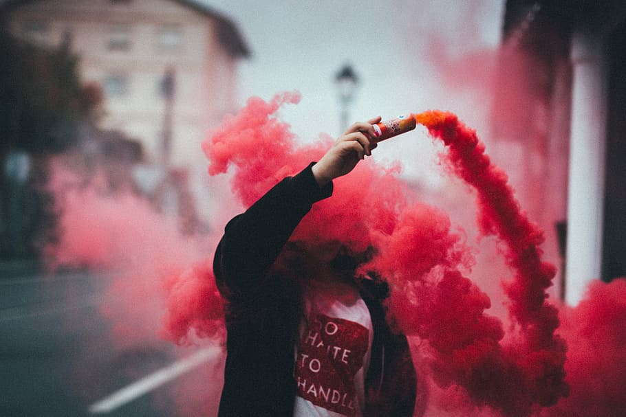 person holding canister with smoke, man holding can with red smoke