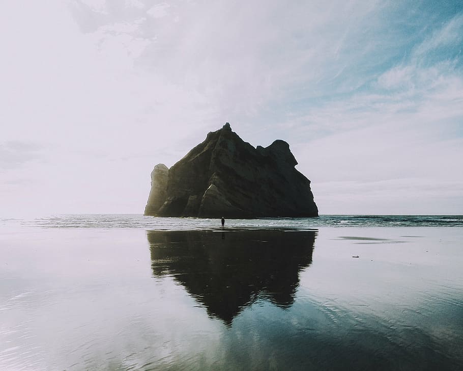 person standing in front of gray islet on seashore, rocky, mountain HD wallpaper