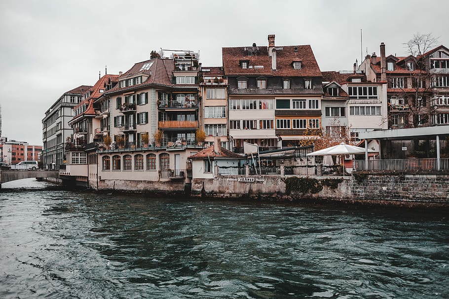 concrete structures near body of water, body of water next to white and brown buildings under white cloudy sky at daytime HD wallpaper
