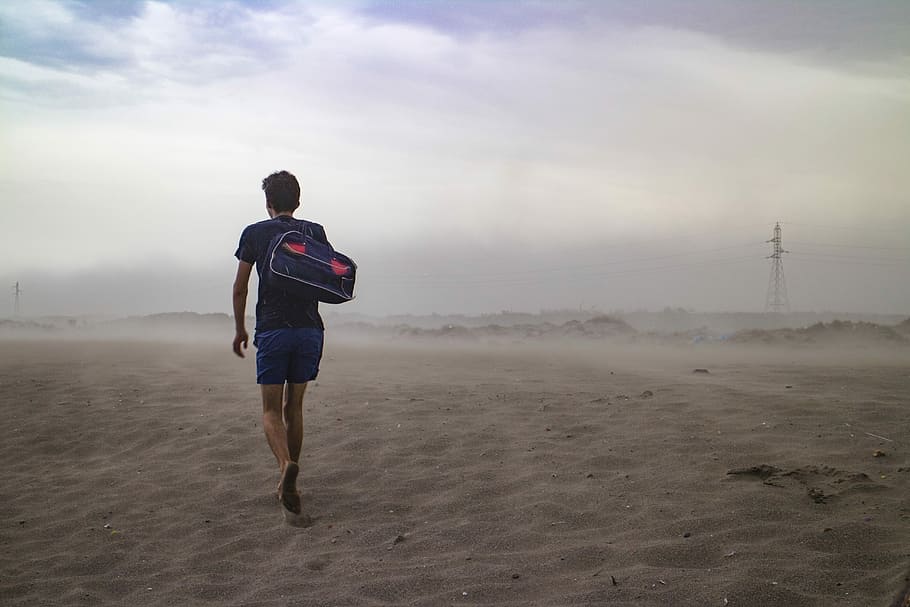 man wearing black t-shirt and blue short carrying black duffel bag on shoulder in the middle of desert, man holding duffel bag and walking on white sand HD wallpaper