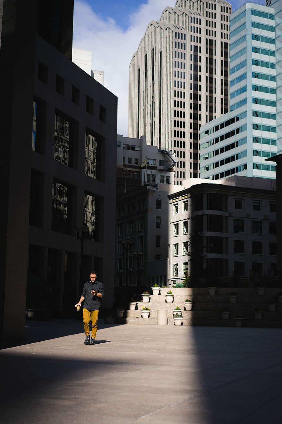 man standing beside building, man walking while using phone, city