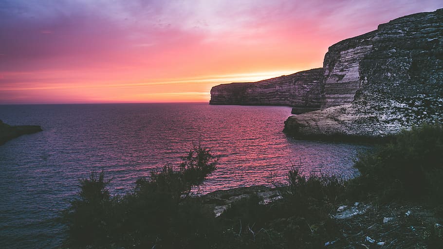 photography of ocean and rock formation at golden hour, gray and black cliff near body of water during dawn HD wallpaper