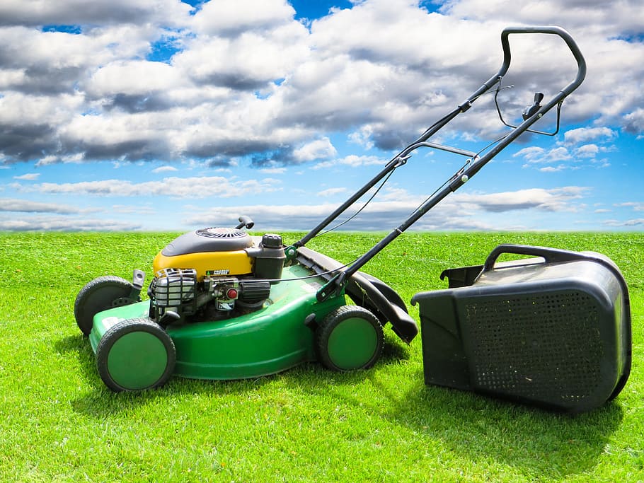 green and yellow push mower on green grass field under clouded sky