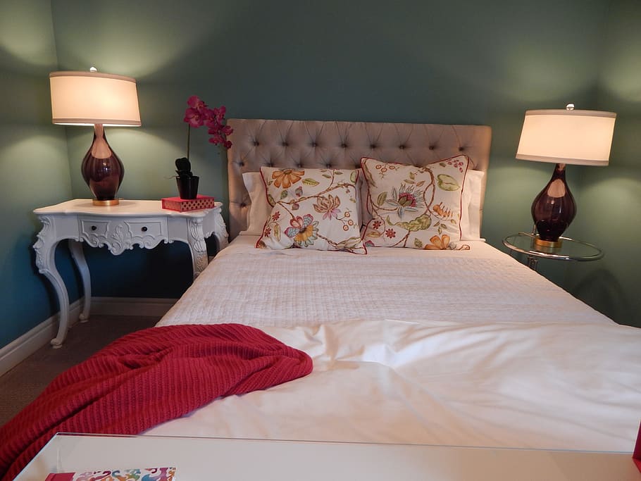 bed with red blanket on the side and table lamps turned on, bedroom