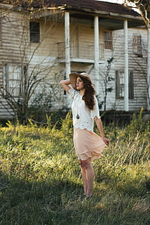 woman wearing gray sun hat, white shirt and peach-colored skirt standing in green grass and white wooden house HD wallpaper