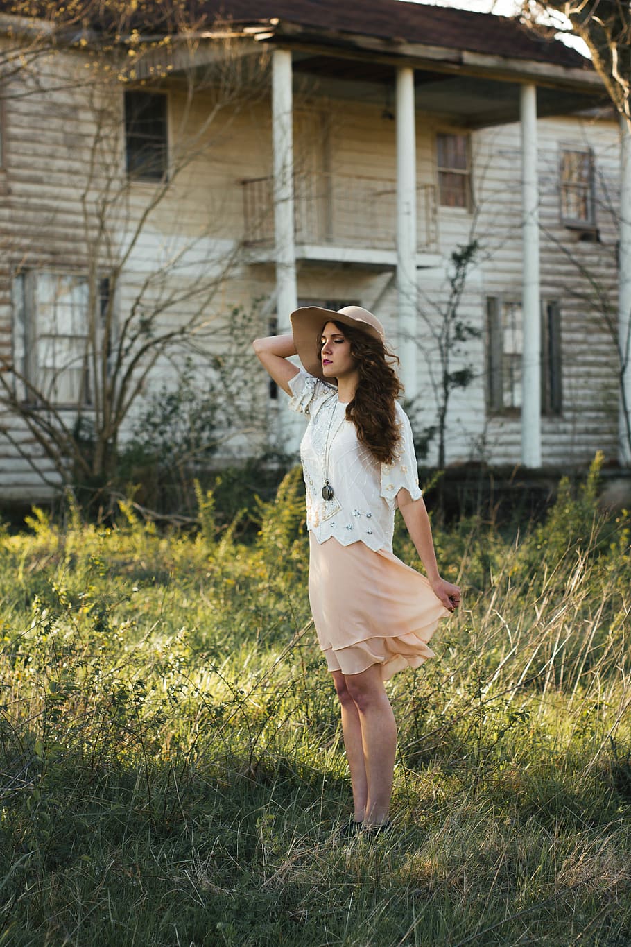 woman wearing gray sun hat, white shirt and peach-colored skirt standing in green grass and white wooden house HD wallpaper