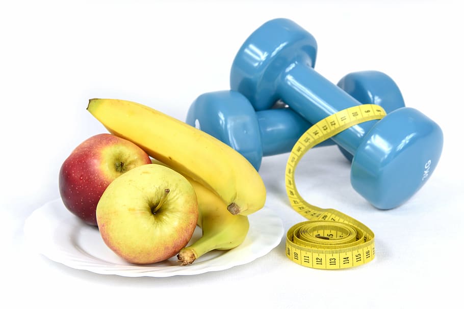 two apples and two bananas served on white plate near two blue fixed weight dumbbells and tape measure