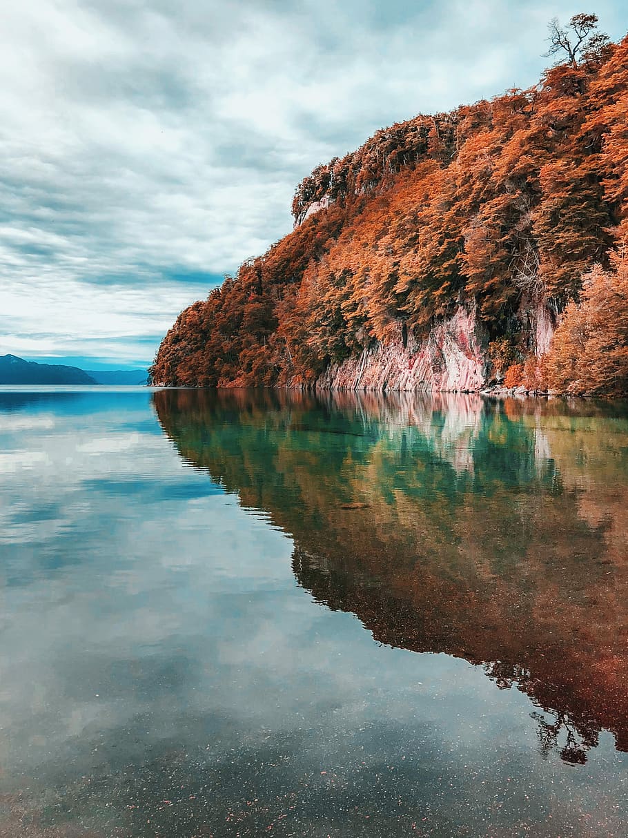 lake alps under cloudy sky at daytime, calm waters near rock cliffs and brown leaved trees HD wallpaper
