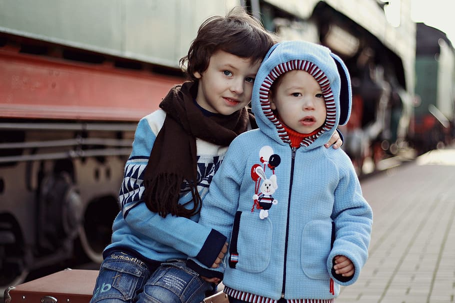 boy sitting beside another boy in blue zip-up hoodie standing outdoors HD wallpaper