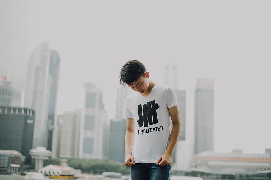 man looking at his shirt with buildings background, boy standing near buildings