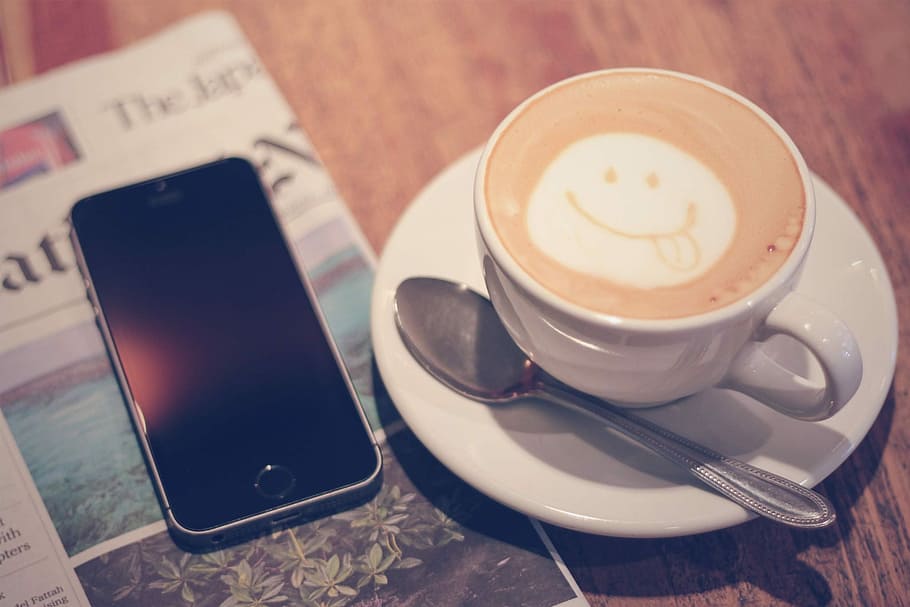 space gray iPhone 5s beside white ceramic teacup with latte, coffee - Drink