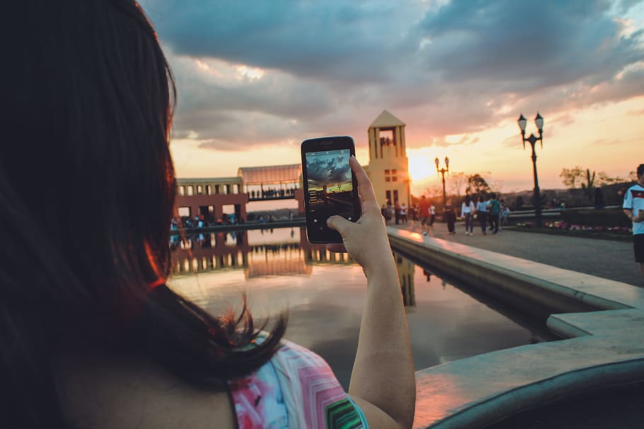Woman Holding Smartphone Capturing Sunset, architecture, blur HD wallpaper