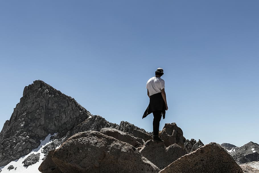 man standing on rock mountain peak, person standing on gray rock formation HD wallpaper