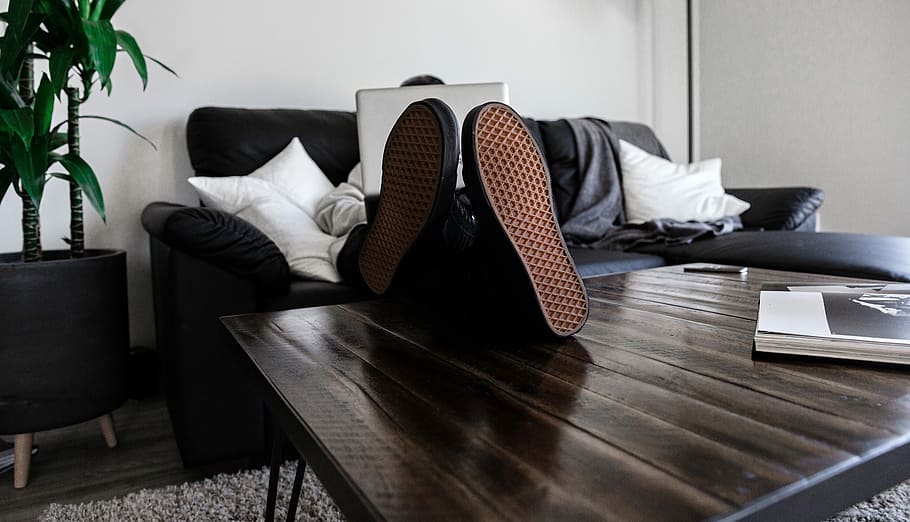 person sitting on sofa resting its feet on top of coffee table while using laptop, person wearing black sneakers on top of table inside the room HD wallpaper