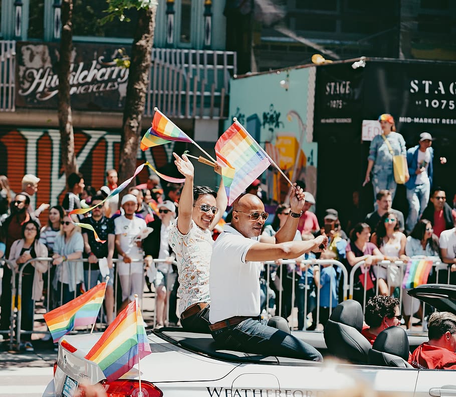 four men riding on car parade, two men riding a convertible coupe holding LGBT flaglets during daytime HD wallpaper