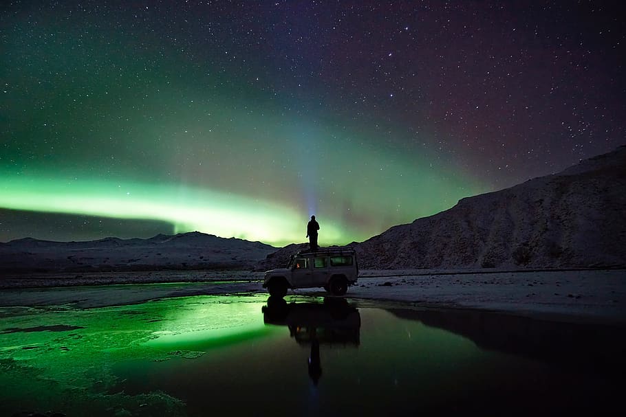 person standing on top of SUV in front on mountain during nighttime HD wallpaper