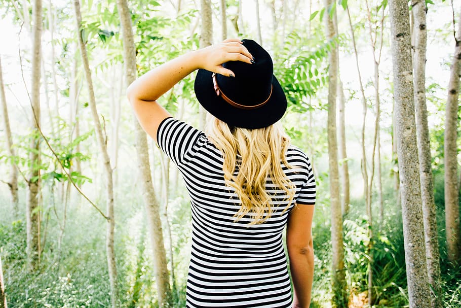 Woman in a bright forest, woman in black and white striped shirt wearing black cap standing in a forest
