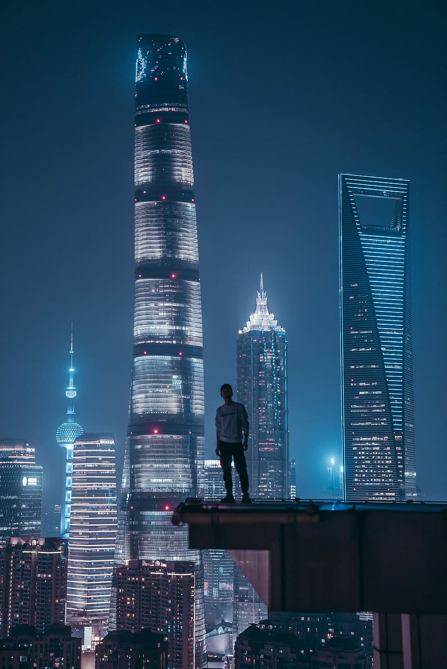 man standing on top of skyscraper, man standing on top of building during nighttime