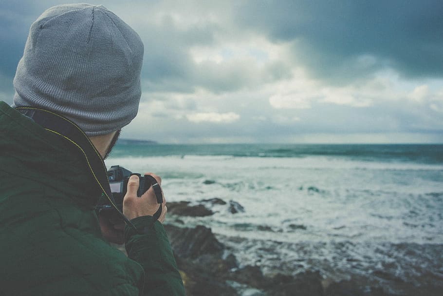 man holding DSLR camera taking picture of beach waves, man taking photo of ocean wave during gray clouds HD wallpaper