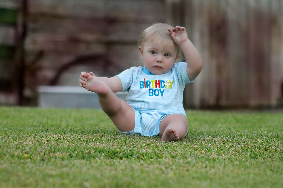 close up photography of boy sitting on grass field, baby, in blue