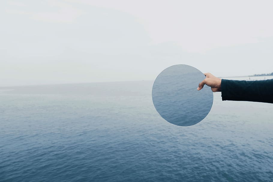 person holding glass top, person holding round mirror beside body of water HD wallpaper