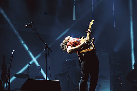 person wearing orange t-shirt playing electric guitar on stage HD wallpaper