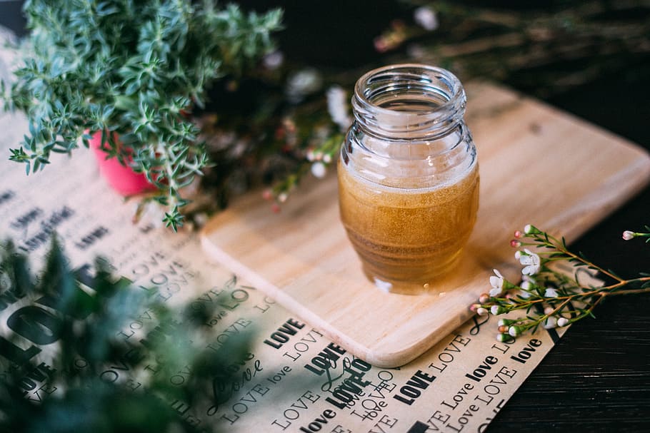 shallow focus photography clear glass jar on chopping board, clear glass cup with liquid on brown wooden chopping board beside plant HD wallpaper