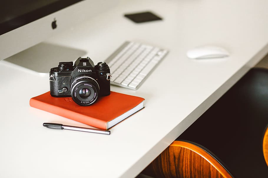 black Nikon DSLR camera on red notepad, black Nikon DSLR camera on top of orange book HD wallpaper