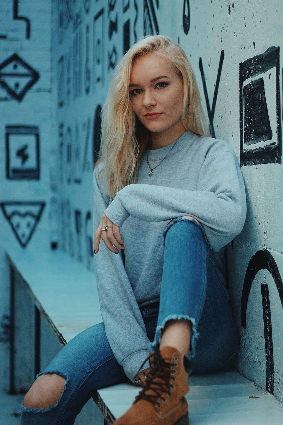 woman in sweatshirt, distressed jeans, and brown lace-up boots sitting with forearm resting on left lap HD wallpaper