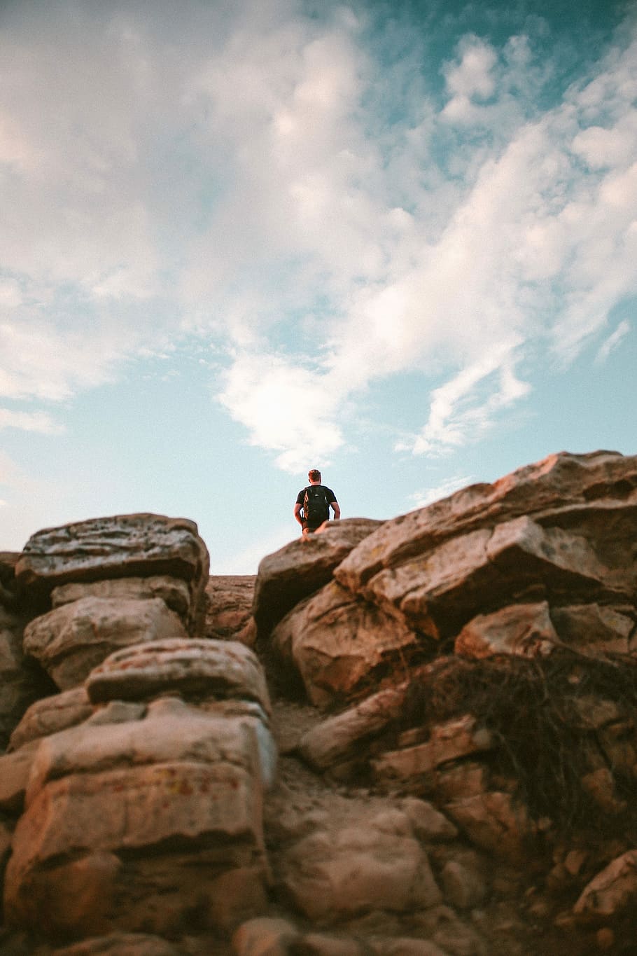 low-angle photography of man standing on brown cliff under clear blue sky during daytime, man standing on brown rock mountain HD wallpaper